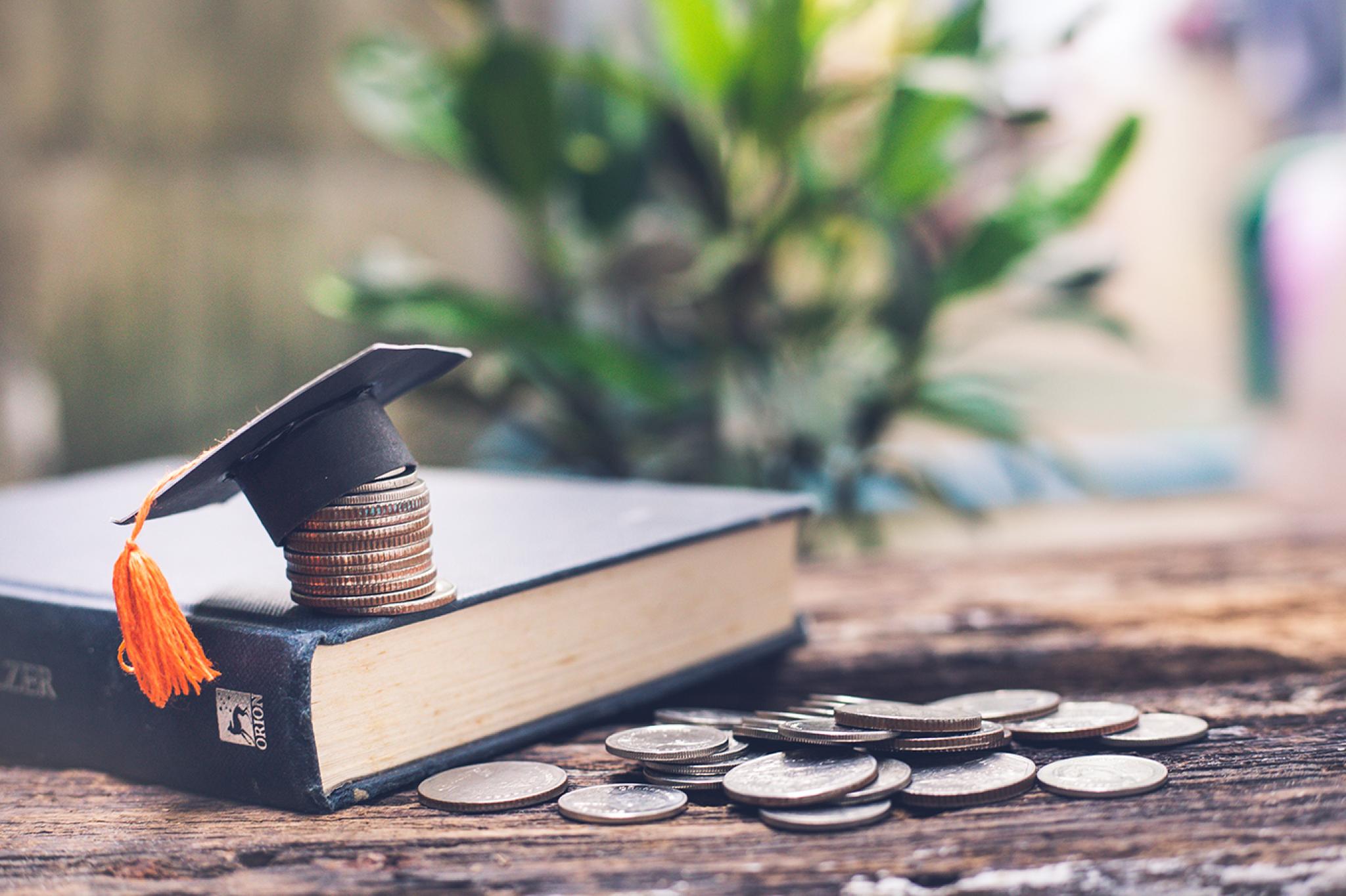 Graduates cap on top of the money with book. By Adobe stock