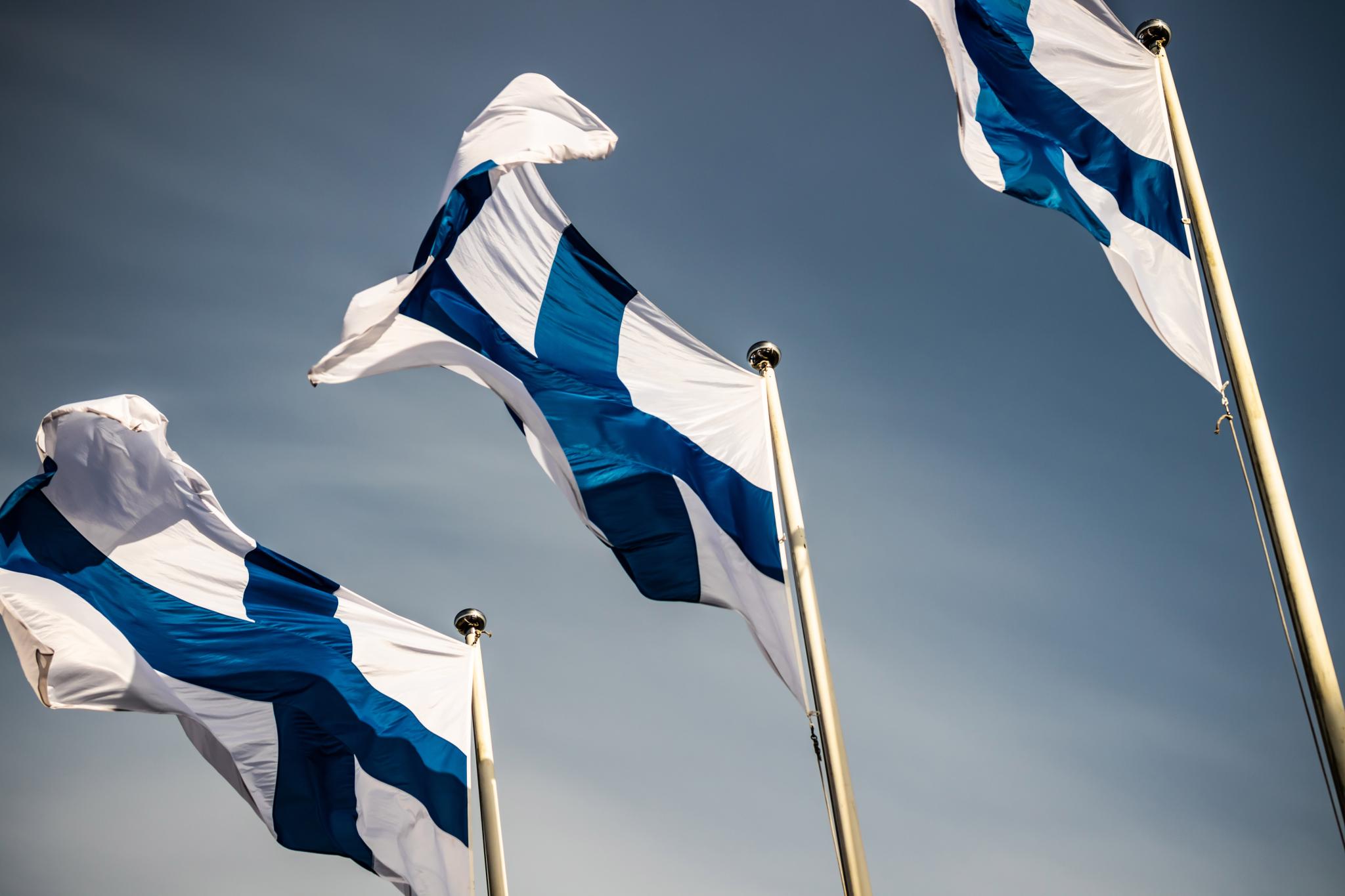 Three finnish national flags on the wind against the blue sky 