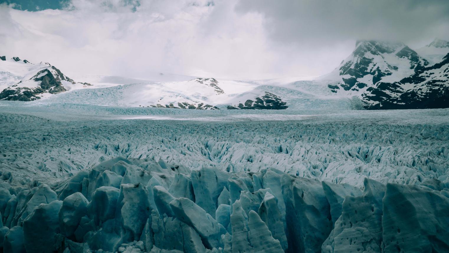 Picture of glaciers in Antartica with snowy rock mountains in the background